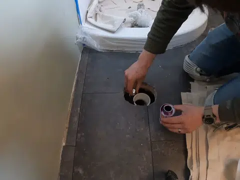 Installer setting a drain opening in tiled bathroom floor for index in Stanton shown from a different service angle