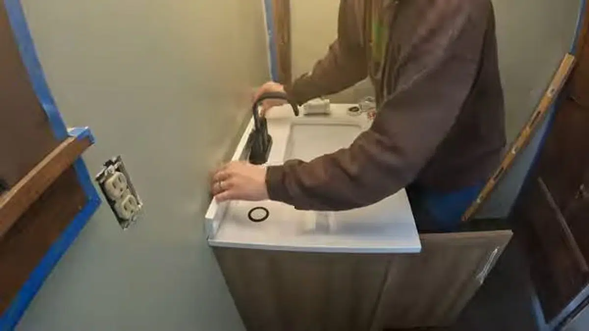 Installer connecting wall-mounted sink plumbing in remodel for toilet repair installation in Stanton