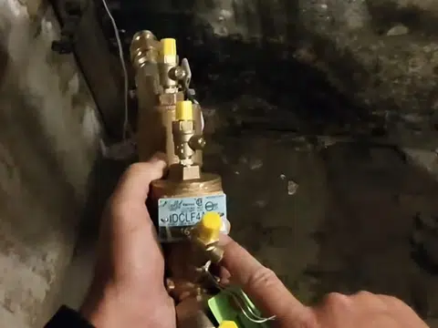 Hand holding brass gas shutoff valve in utility area for index in Stanton