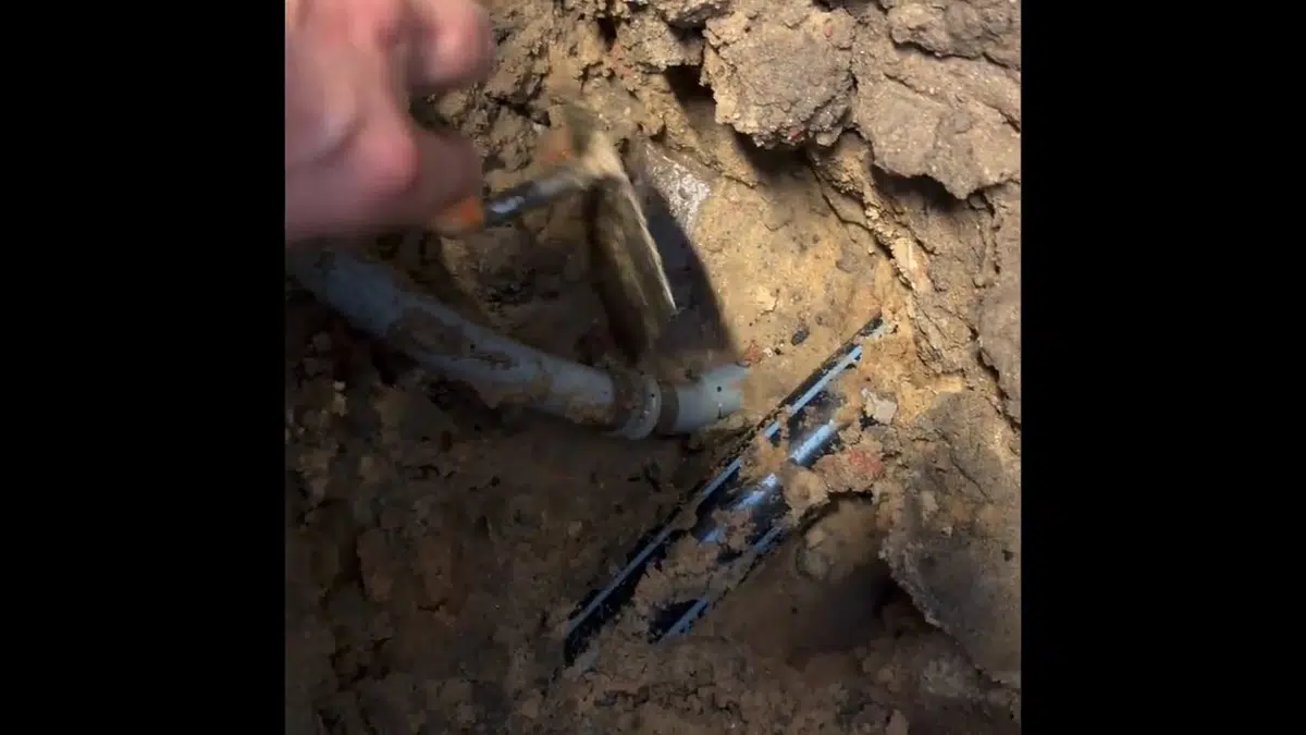 Exposed broken pipe in dirt beside slab opening for burst pipe repair in Stanton