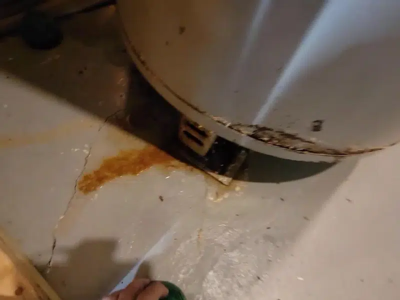 Rust-colored water leaking near bottom of old heater for water heater repair in Stanton