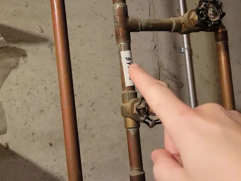 Hand pointing at old copper water heater supply lines for gas line in Stanton