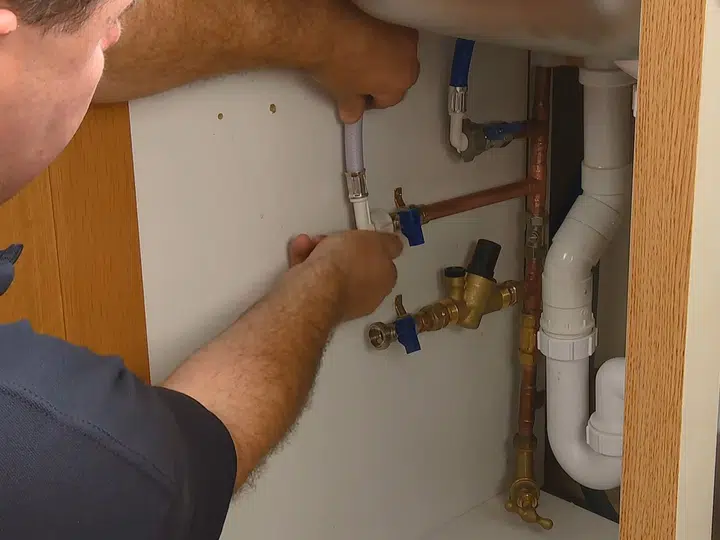Technician working below sink on water softener connections for faucet sink repair in Stanton